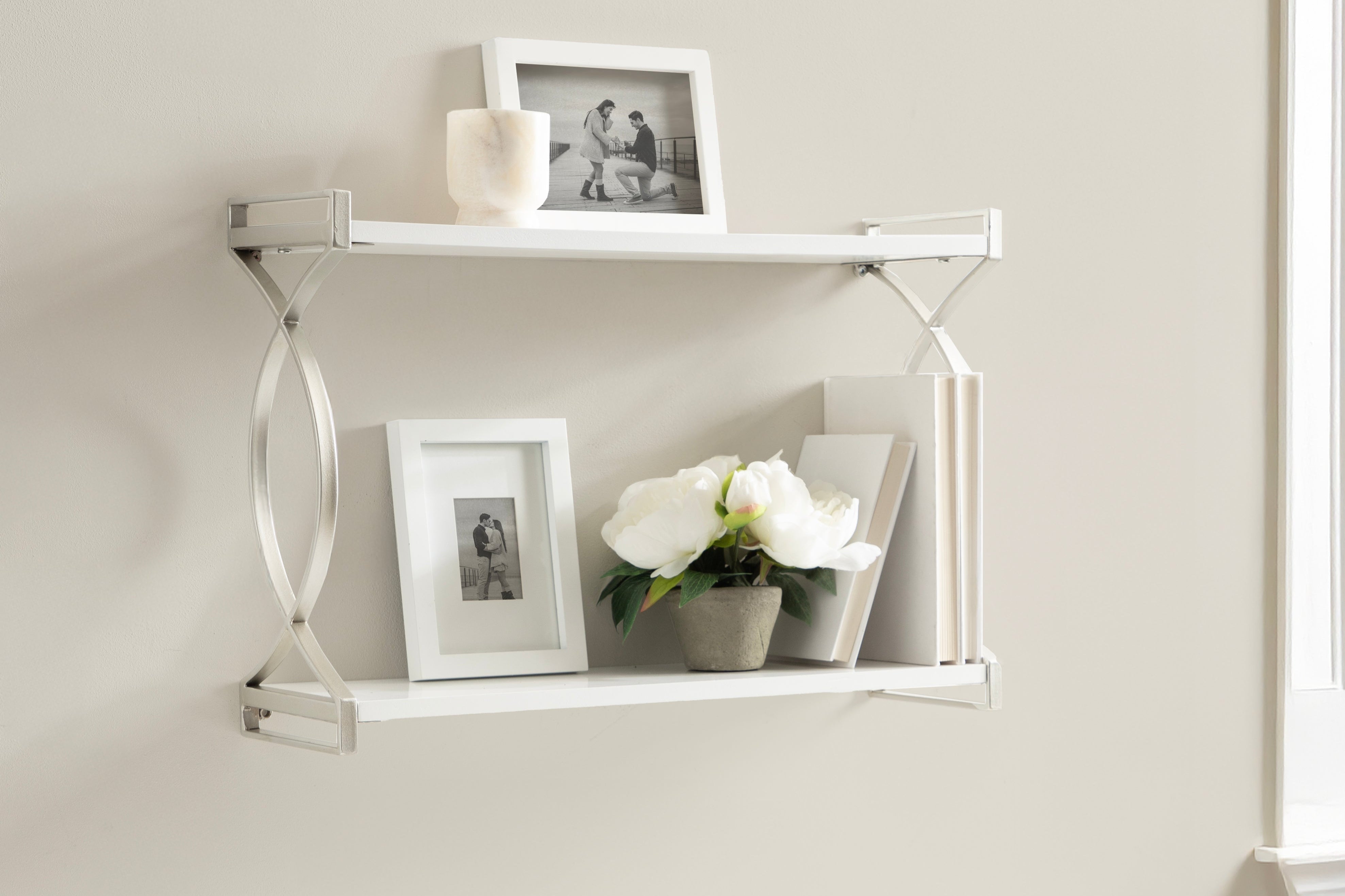 White desk with a shelf above, featuring a plant, books, and photos.