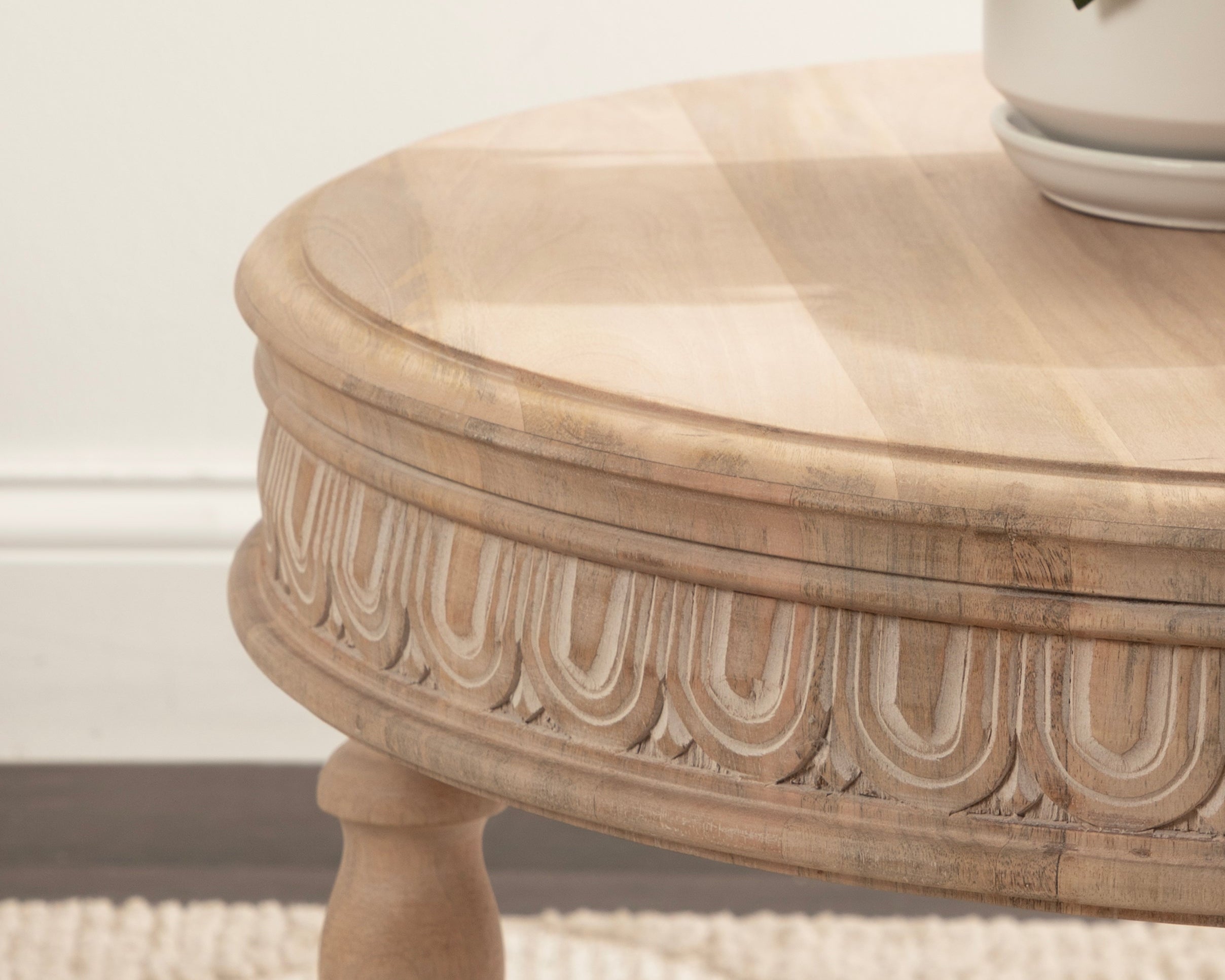 Round wooden side table with decorative carvings on a textured surface.