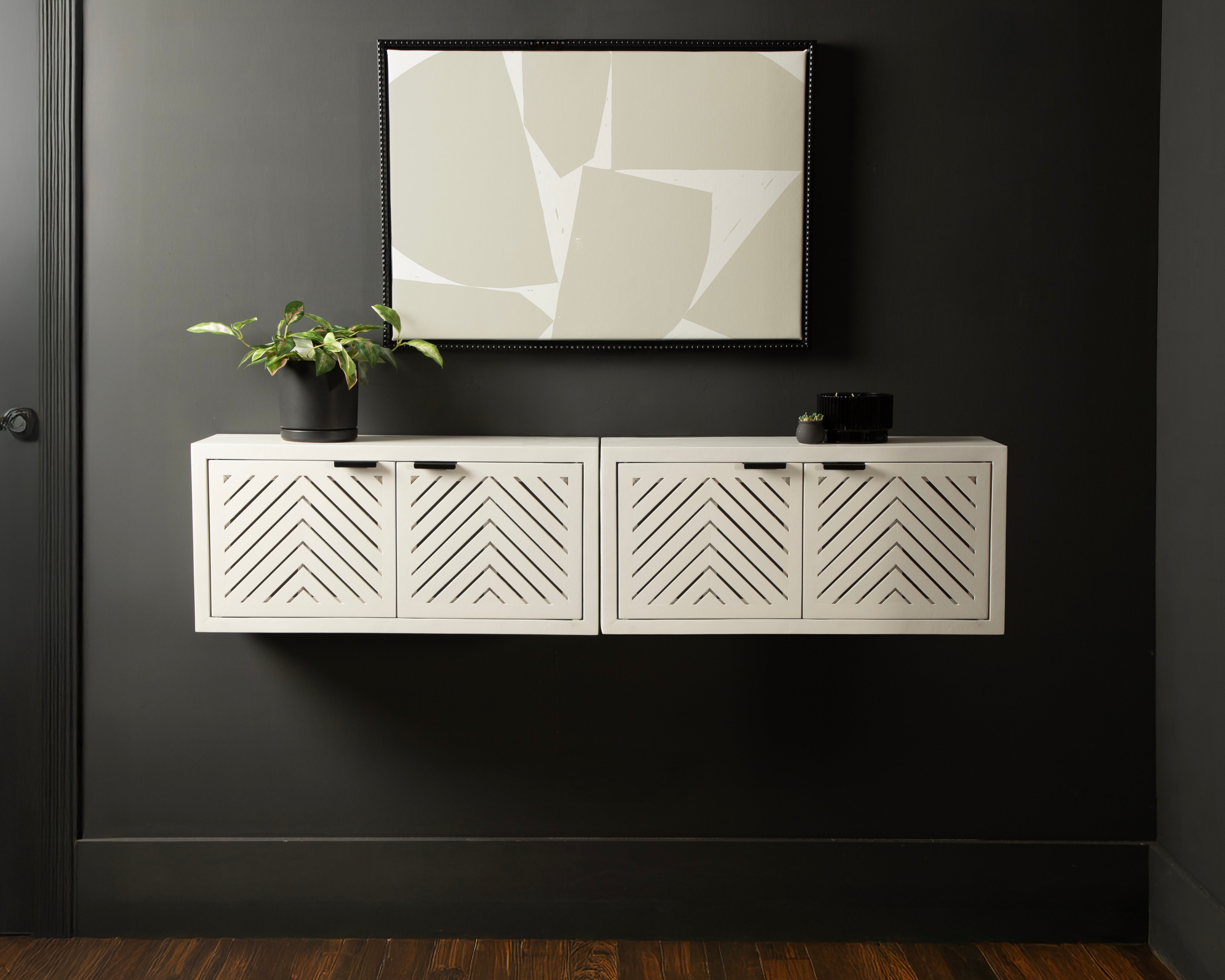 White wall-mounted cabinet with geometric patterns against a dark wall with abstract art.