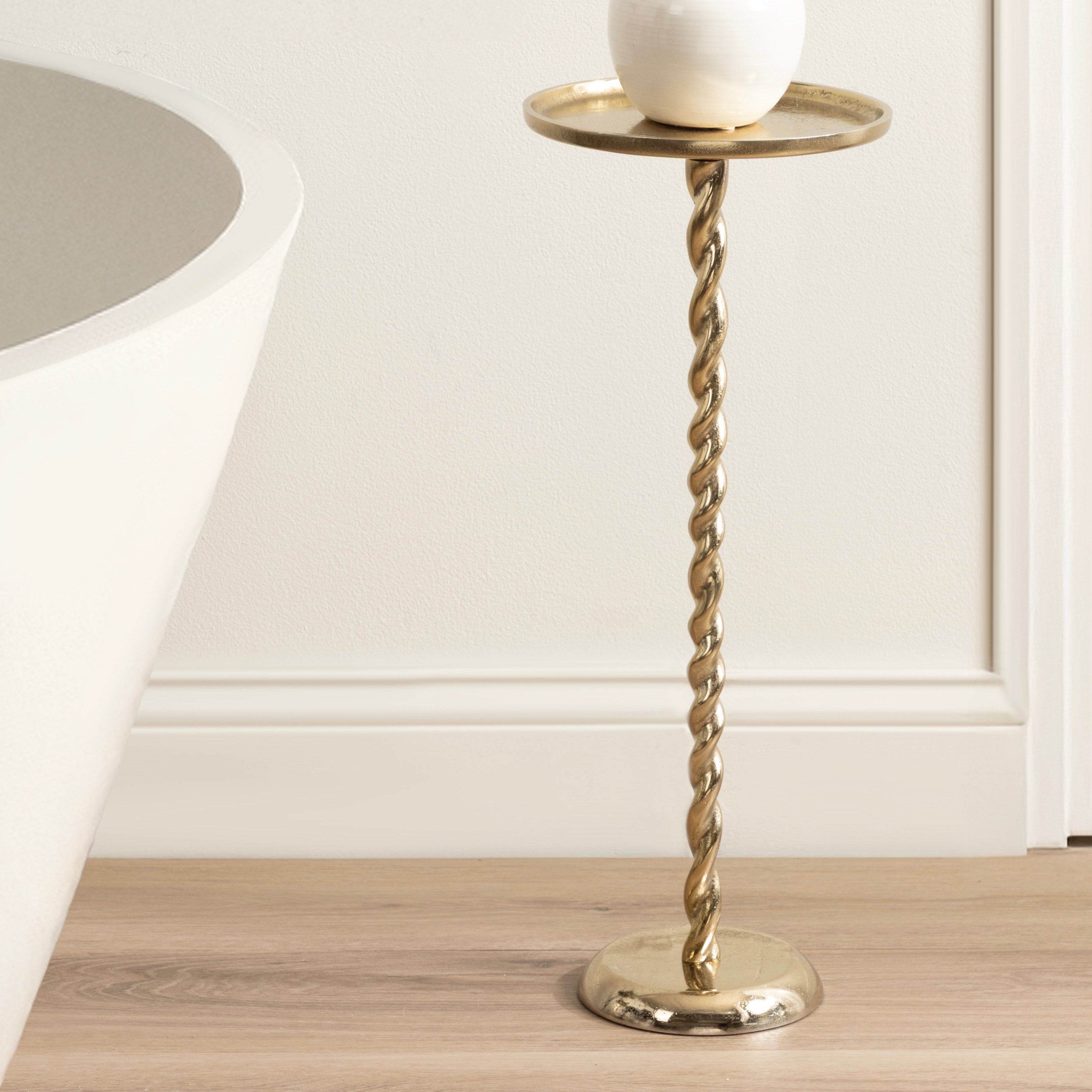 Tall gold twisted metal side table with a white vase and decorative items on a wooden floor.