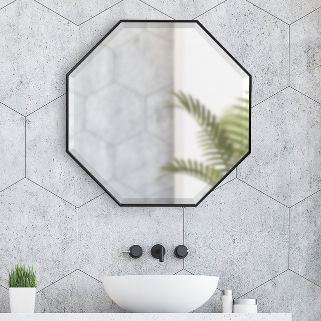 Octagonal mirror on a gray tiled wall with a white sink and decorative elements.