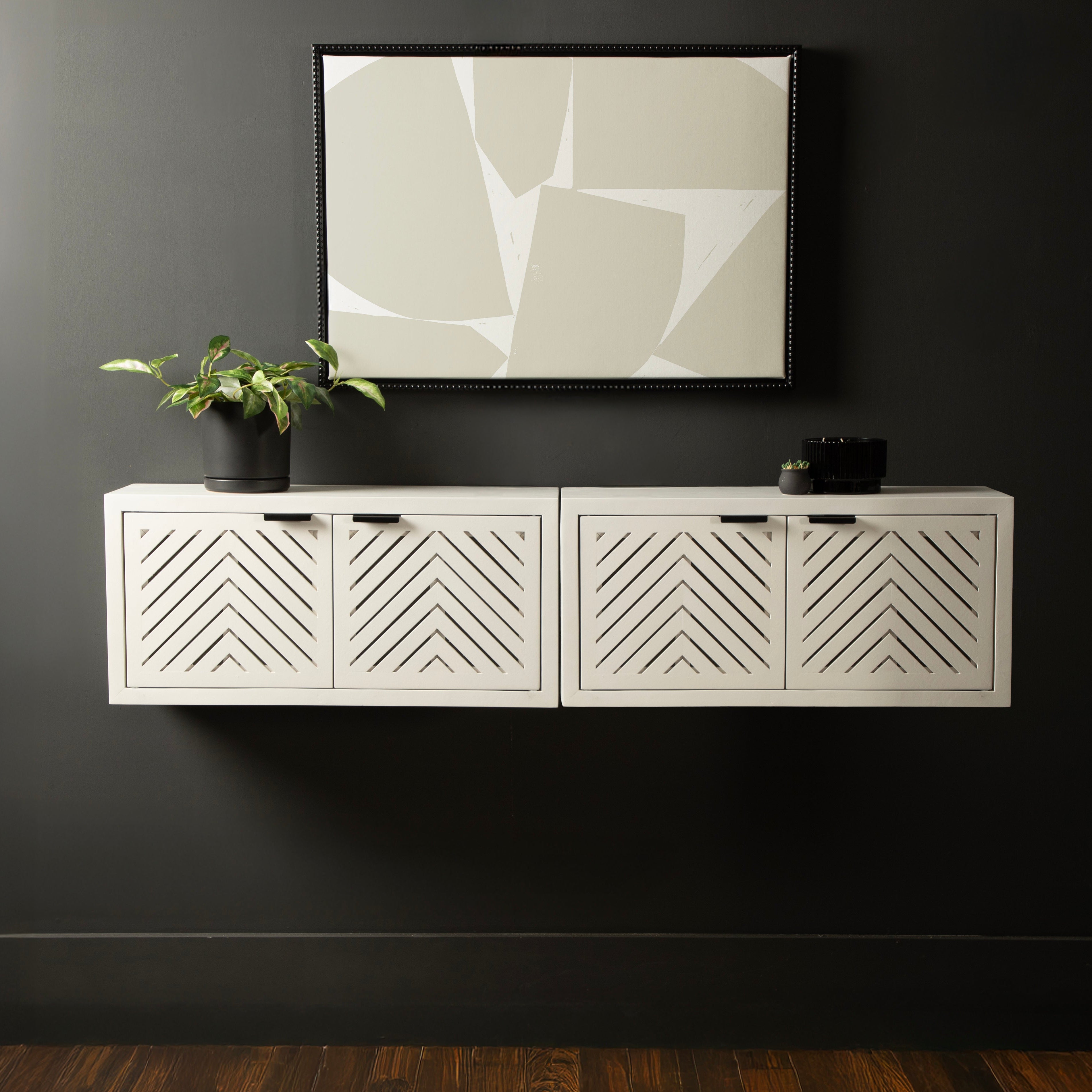 White wall-mounted cabinet with geometric patterns against a dark wall with abstract art.