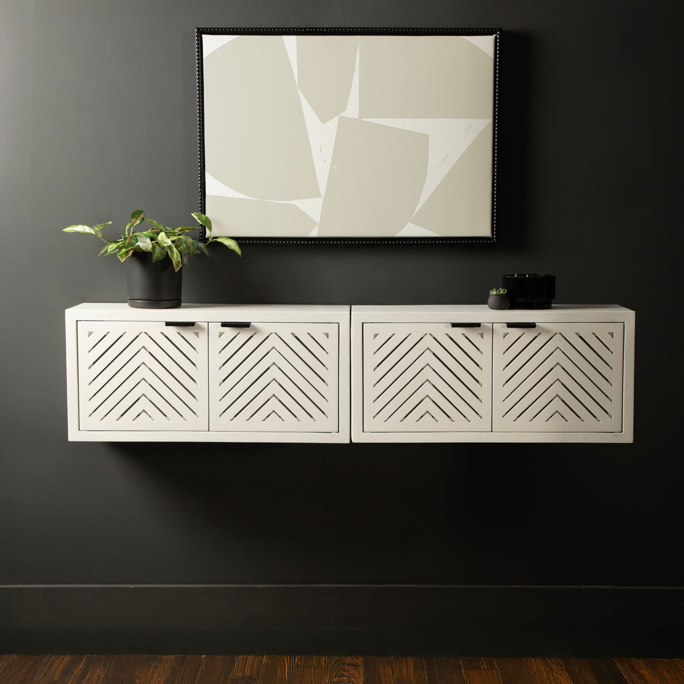 White wall-mounted cabinet with geometric patterns against a dark wall with abstract art.
