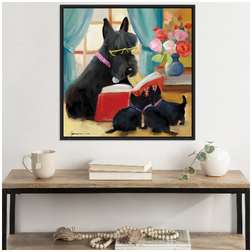 A framed canvas art print featuring a painting of a large black dog with glasses and two smaller dogs wearing pink collars, sitting in front of a book with a colorful background including flowers and a blue curtain.