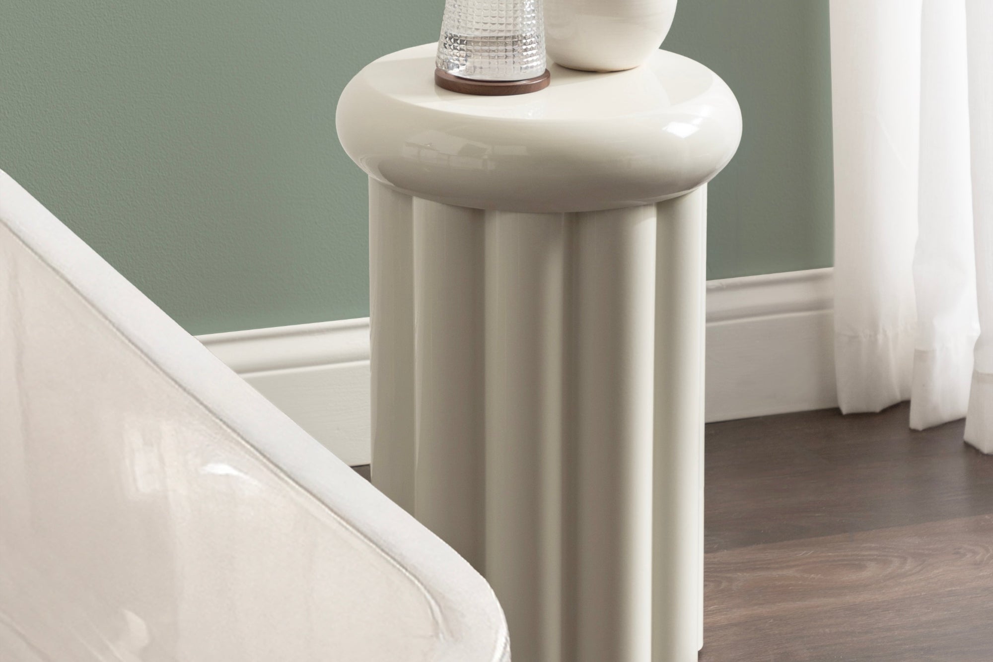 Round white side table with decorative items against a green wall.