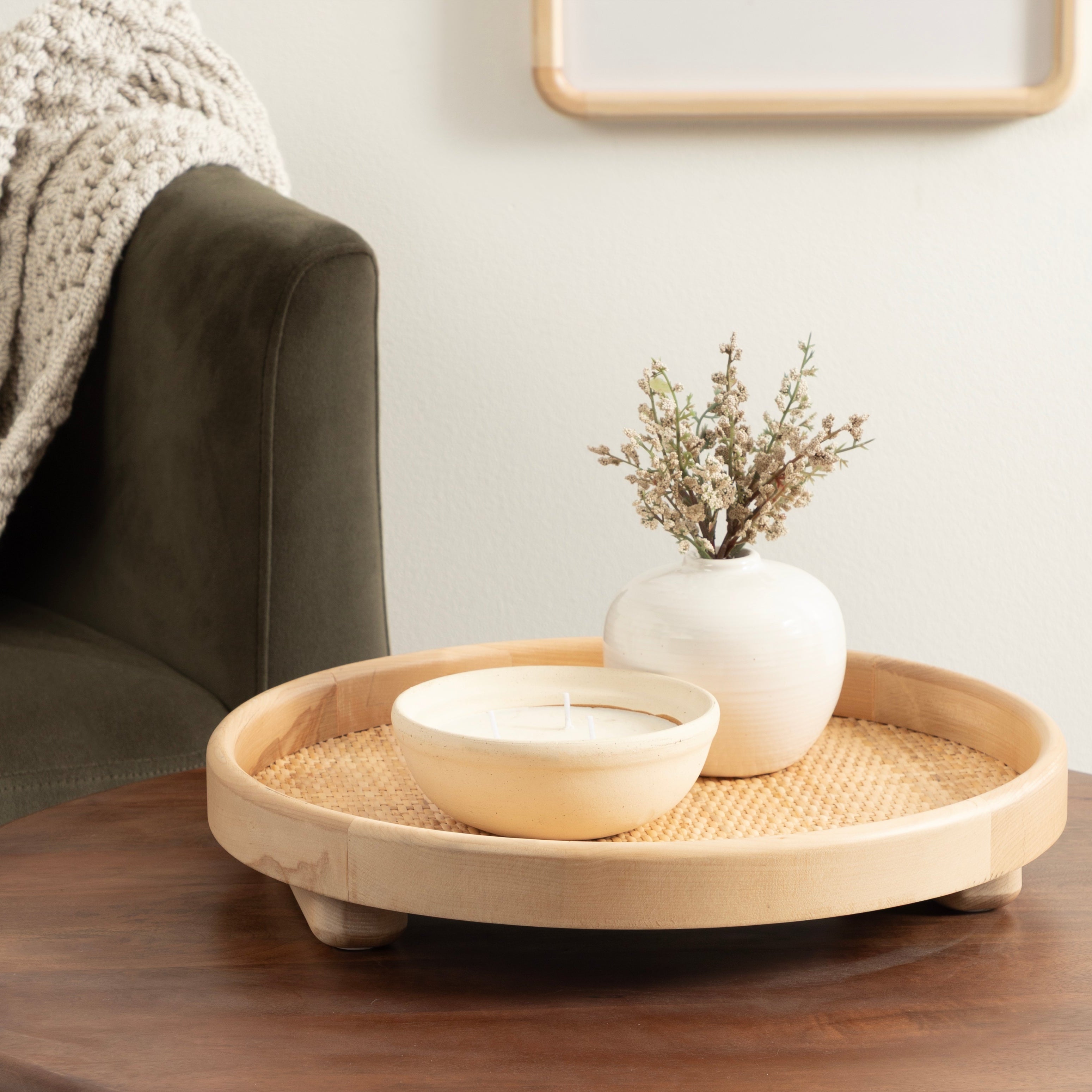 Round wooden tray with a white vase and bowl on a wooden table in a living room setting.