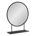A round tabletop mirror with a black metal frame, designed to be freestanding on a flat surface.