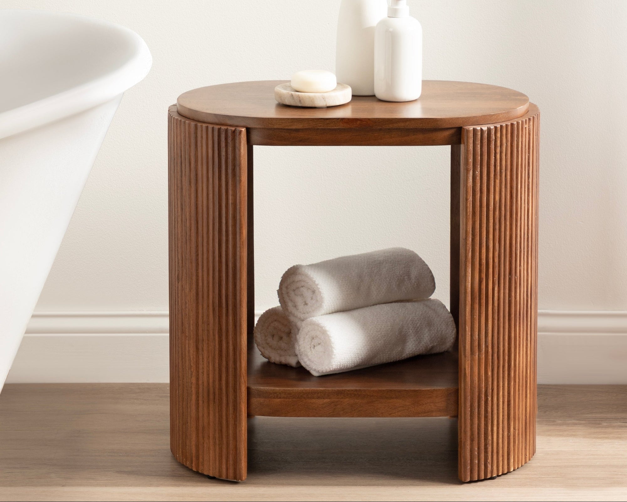 Wooden side table with a vase of greenery and rolled towels in a bathroom setting