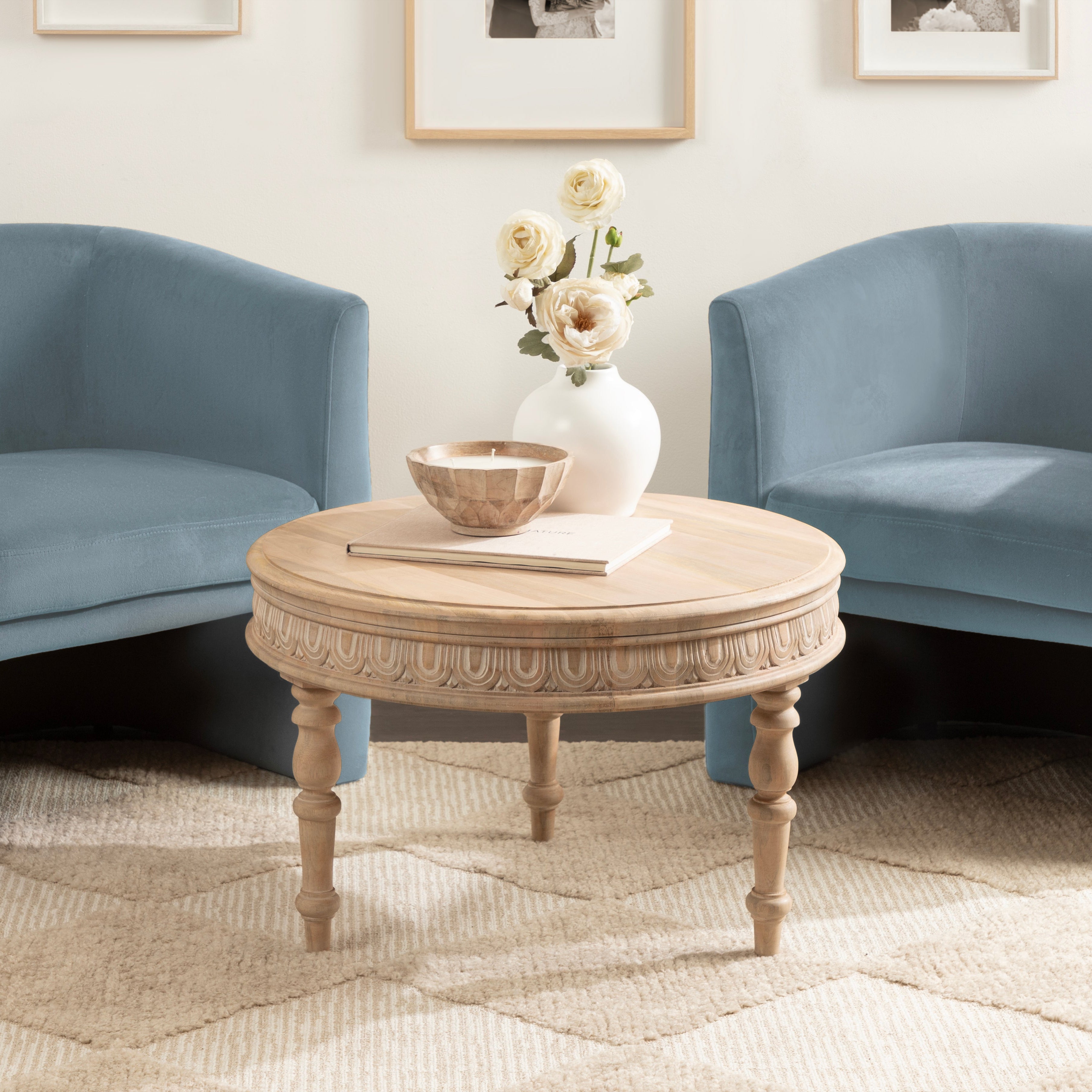 Round wooden coffee table with decorative items in a living room with blue armchairs.