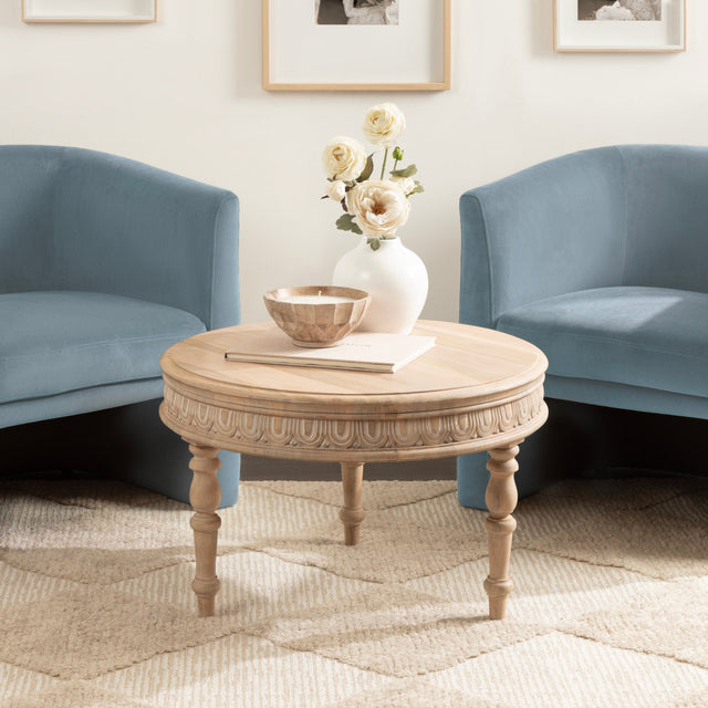 Round wooden coffee table with decorative items in a living room with blue armchairs.