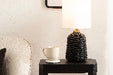 Black side table with a lamp, mug, and books next to a gray sofa.