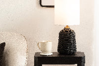 Black side table with a lamp, mug, and books next to a gray sofa.